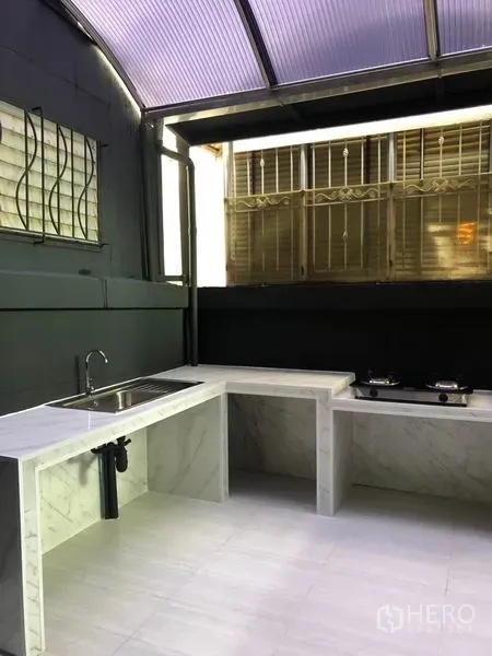 Townhouse for rent in Bang Kapi, Bangkok - Covered Thai kitchen with marble countertops, sink, gas stove and grilled windows.