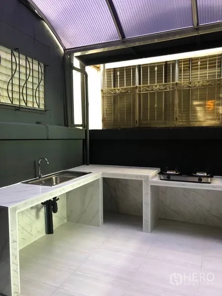 Townhouse for rent in Bang Kapi, Bangkok - Covered Thai kitchen with marble countertops, sink, gas stove and grilled windows.