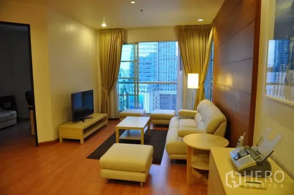 Condominium for rent or sale in Khlong Toei, Bangkok - Bright living room with beige sofa set, TV console, wood floors and balcony window with city view.