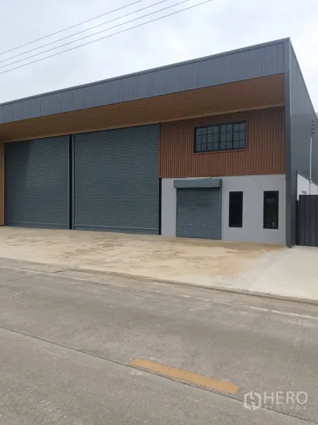 Warehouse for rent in Lam Luk Ka, Pathum Thani - Closer view of the facade showing high roller doors, a smaller loading door, and an office window.