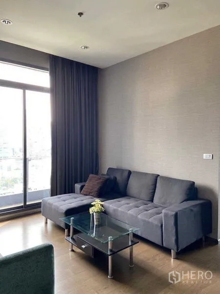公寓 出售在Bang Rak, Bangkok - 客厅采光明亮，深色沙发、玻璃茶几，落地窗享城市景观。