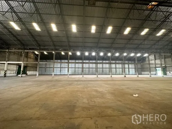 Warehouse for rent in Mueang Pathum Thani, Pathum Thani - Spacious warehouse interior with high steel‑truss roof, skylights and open concrete floor.