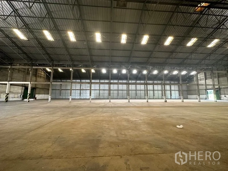 Warehouse for rent in Mueang Pathum Thani, Pathum Thani - Spacious warehouse interior with high steel‑truss roof, skylights and open concrete floor.