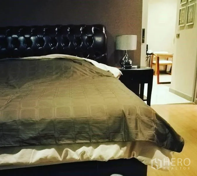 คอนโด ขายในBang Rak, Bangkok - ห้องนอนพร้อมหัวเตียงหนังบุและโคมไฟข้างเตียง พื้นไม้