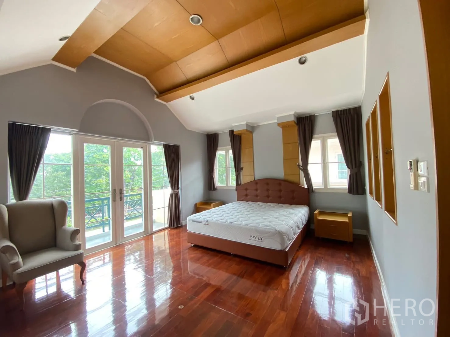 Detached House for rent in Phra Khanong, Bangkok - Master bedroom with vaulted ceiling, French doors to a balcony, windows, bed, and an armchair.