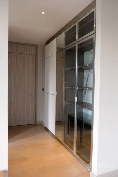 独立式住宅 出租在Watthana, Bangkok - 走廊设有玻璃陈列柜与白色收纳柜，浅色木地板。
