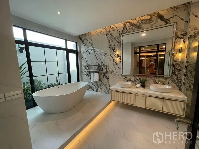 Detached House for rent or sale in Saphan Sung, Bangkok - Luxurious bathroom featuring a freestanding bathtub, marble accent wall and double vanity with large mirror.