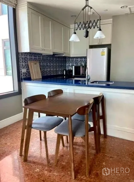 Condominium for rent in Khlong Toei, Bangkok - Dining area beside open kitchen with blue countertop and patterned tile backsplash.