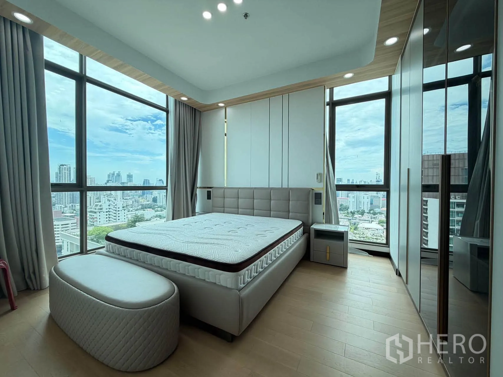 Condominium for sale in Watthana, Bangkok - Bedroom with padded headboard, tall windows, and fitted wardrobes.
