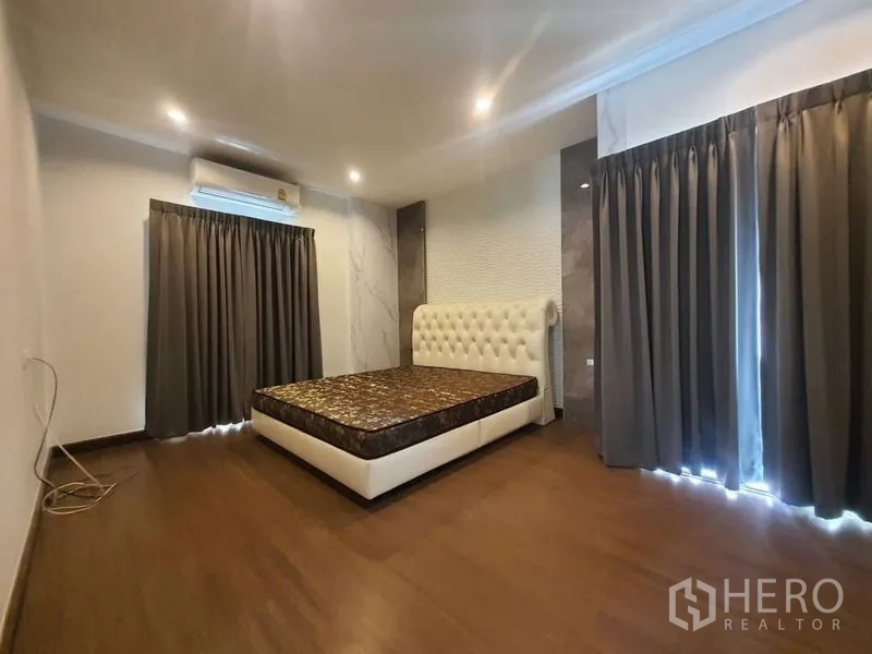 独立式住宅 出租在Prawet, Bangkok - 宽敞卧室，空调、落地窗帘和白色软包床头。