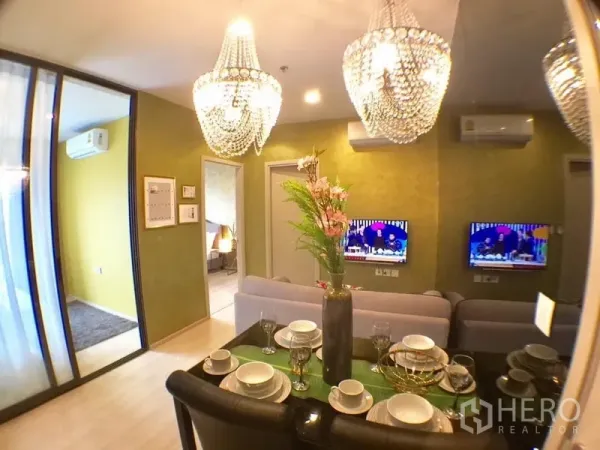 Condominium for rent in Khlong Toei, Bangkok - Open-plan living and dining with crystal chandeliers, mirror wall, sliding glass bedroom door and wall-mounted TV.