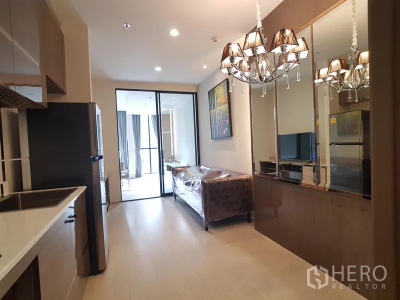 公寓 出租在Pathum Wan, Bangkok - 开放式客厅与小厨房，吊灯与镜面墙，玻璃门通往卧室