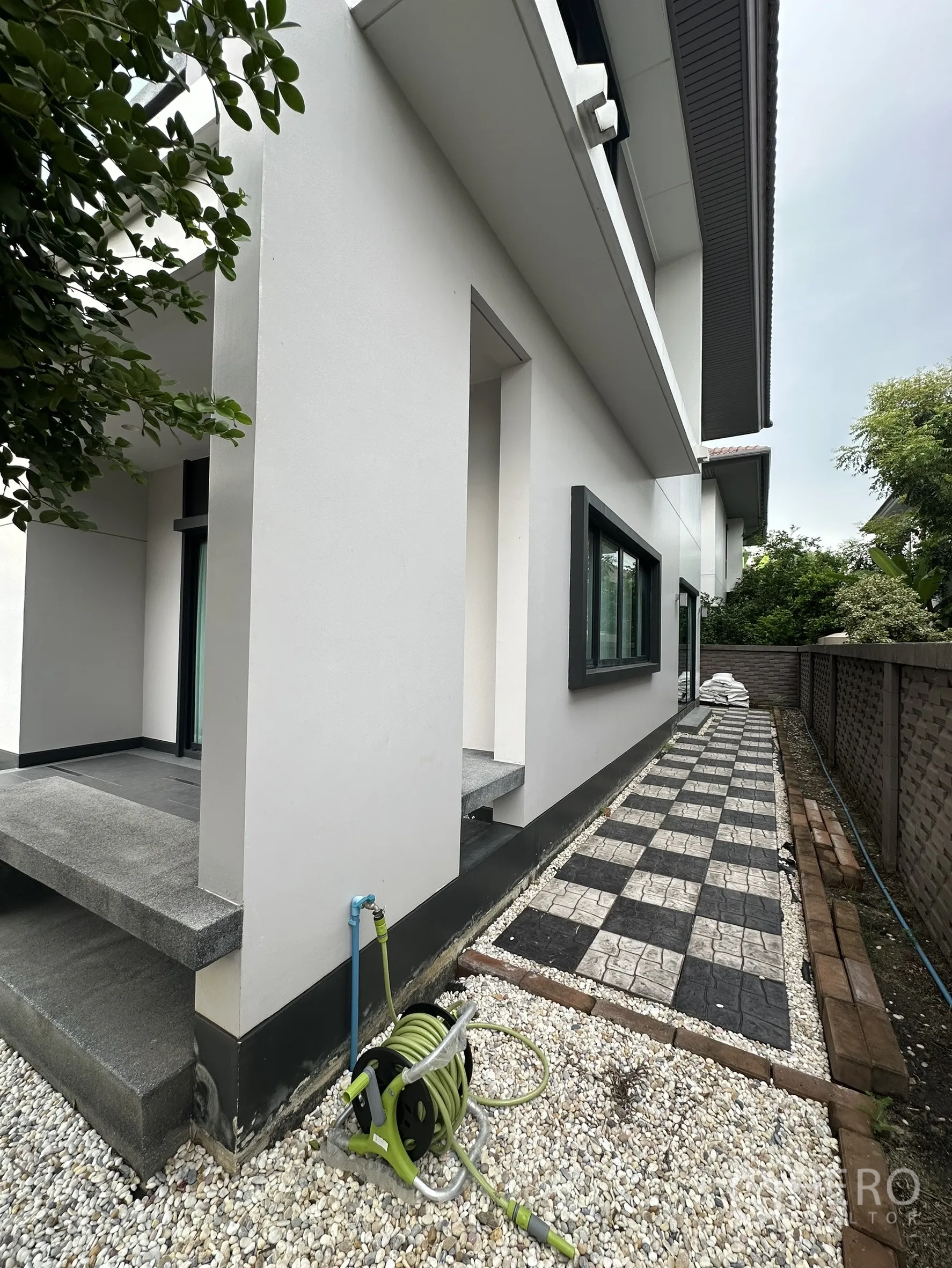 Detached House for rent in Lam Luk Ka, Pathum Thani - Side yard with checkerboard pavers, gravel and garden hose.