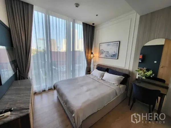 Condominium for rent in Watthana, Bangkok - Cozy bedroom with large windows, queen bed, dressing desk and soft city view through sheer drapes.