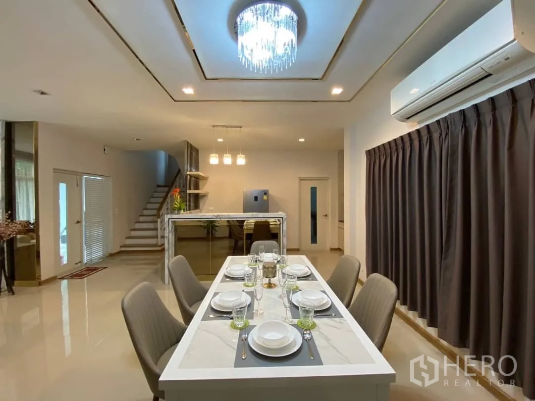 Detached House for rent or sale in Prawet, Bangkok - Dining table under a ceiling crystal light facing the staircase and pantry island.