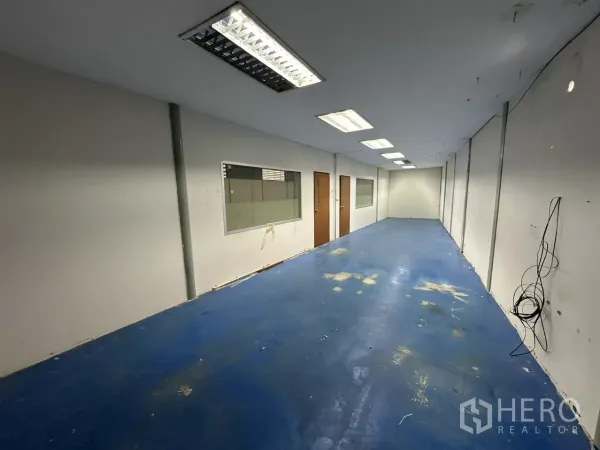 Warehouse for rent in Suan Luang, Bangkok - Long office room featuring blue epoxy floor, fluorescent lighting, and internal windows overlooking the warehouse.