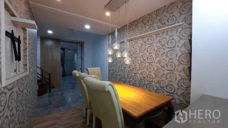 Townhouse for rent or sale in Suan Luang, Bangkok - Dining nook with pendant lighting, feature wallpaper, and wooden table.