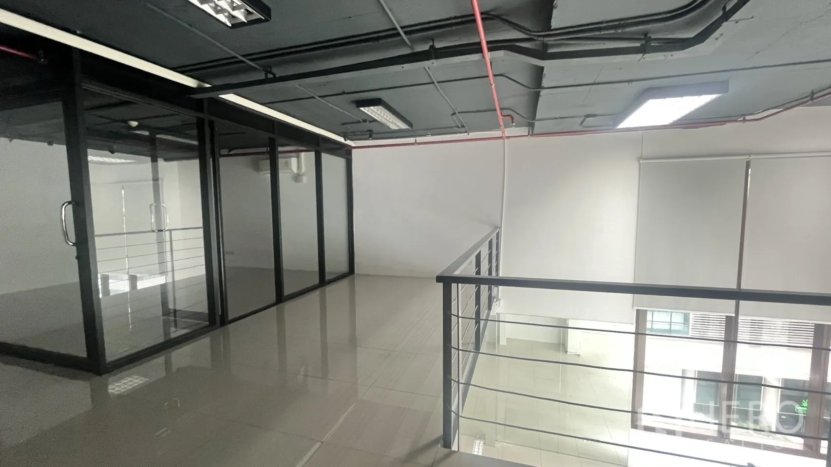 Office Space for rent in Khlong Toei, Bangkok - Glass-partitioned rooms along the mezzanine corridor beside a metal balustrade.