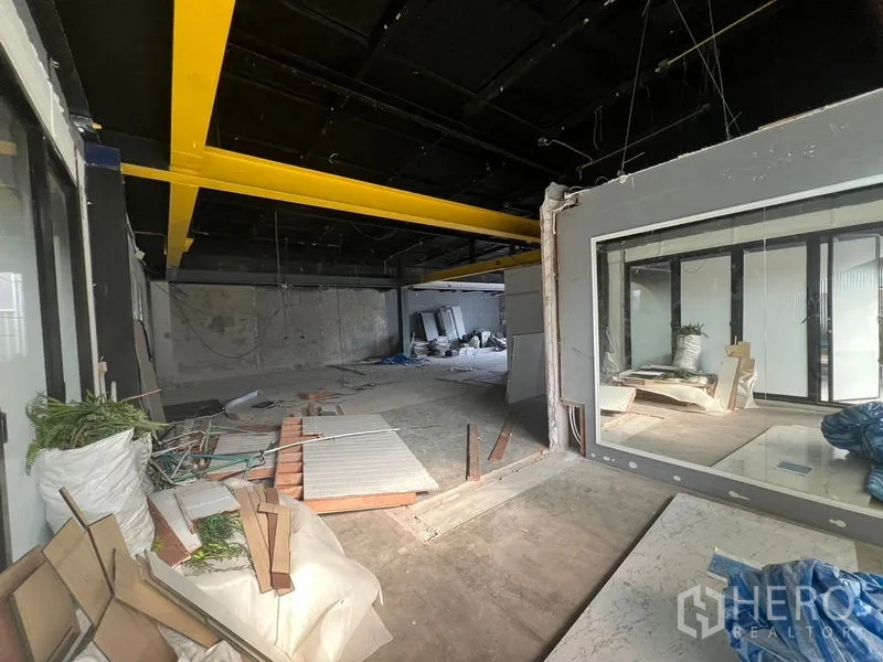 Retail Space for rent in Watthana, Bangkok - Interior zone with bold yellow beams, large internal window partition and debris on floor.