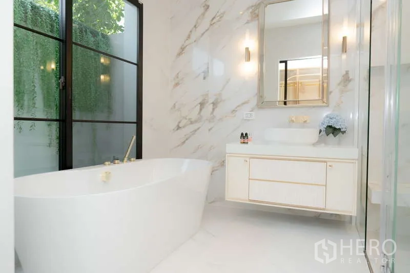 Detached House for rent or sale in Saphan Sung, Bangkok - Luxurious marble bathroom with freestanding bathtub, glass shower and a vanity beneath a large mirror.