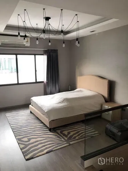 Townhouse for rent in Lat Phrao, Bangkok - Spacious master bedroom with upholstered bed, feature ceiling lights, window and area rug.