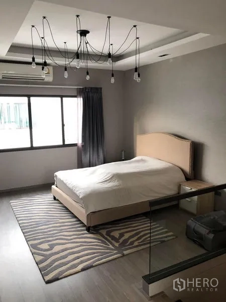 Townhouse for rent in Lat Phrao, Bangkok - Spacious master bedroom with upholstered bed, feature ceiling lights, window and area rug.