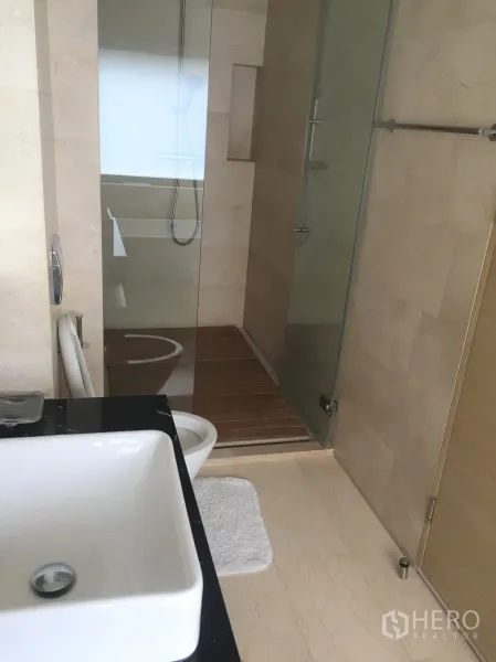 Condominium for rent in Bang Rak, Bangkok - Second bathroom with glass-enclosed shower, square basin and light marble flooring.