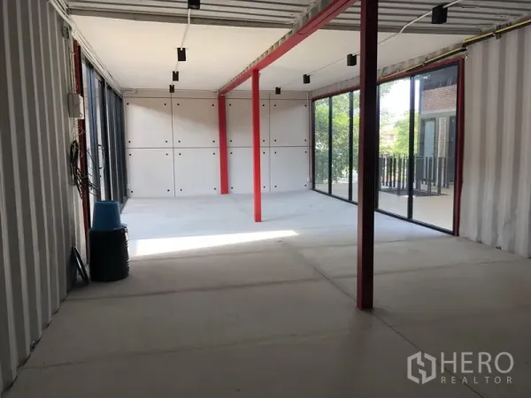 办公空间 出租在Khlong Toei, Bangkok - 转角办公区，双面落地窗、红色立柱、水泥地面，可见阳台与绿意。