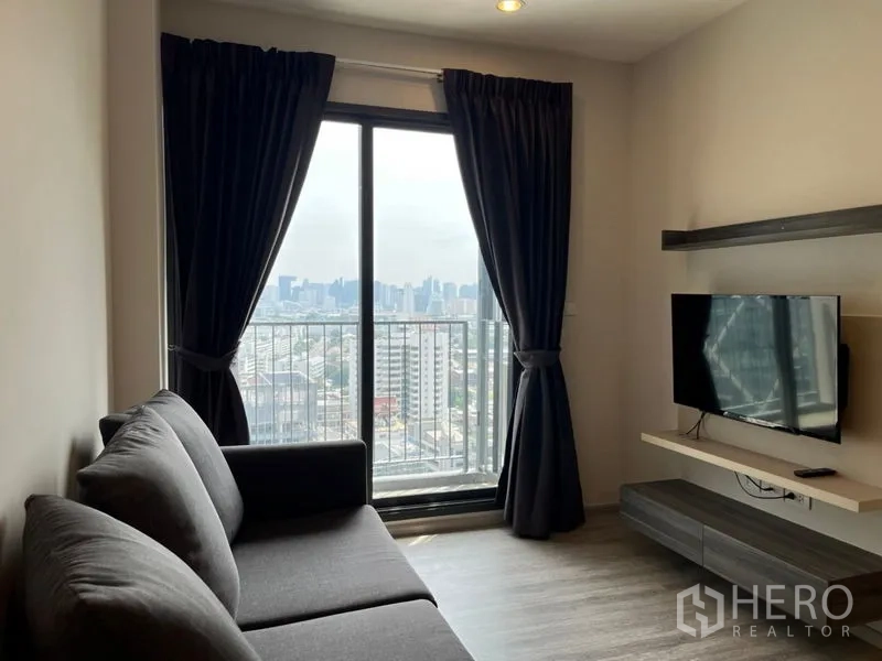 Condominium for sale in Phaya Thai, Bangkok - Living room with sofa, wall-mounted TV and balcony sliding door overlooking the city.