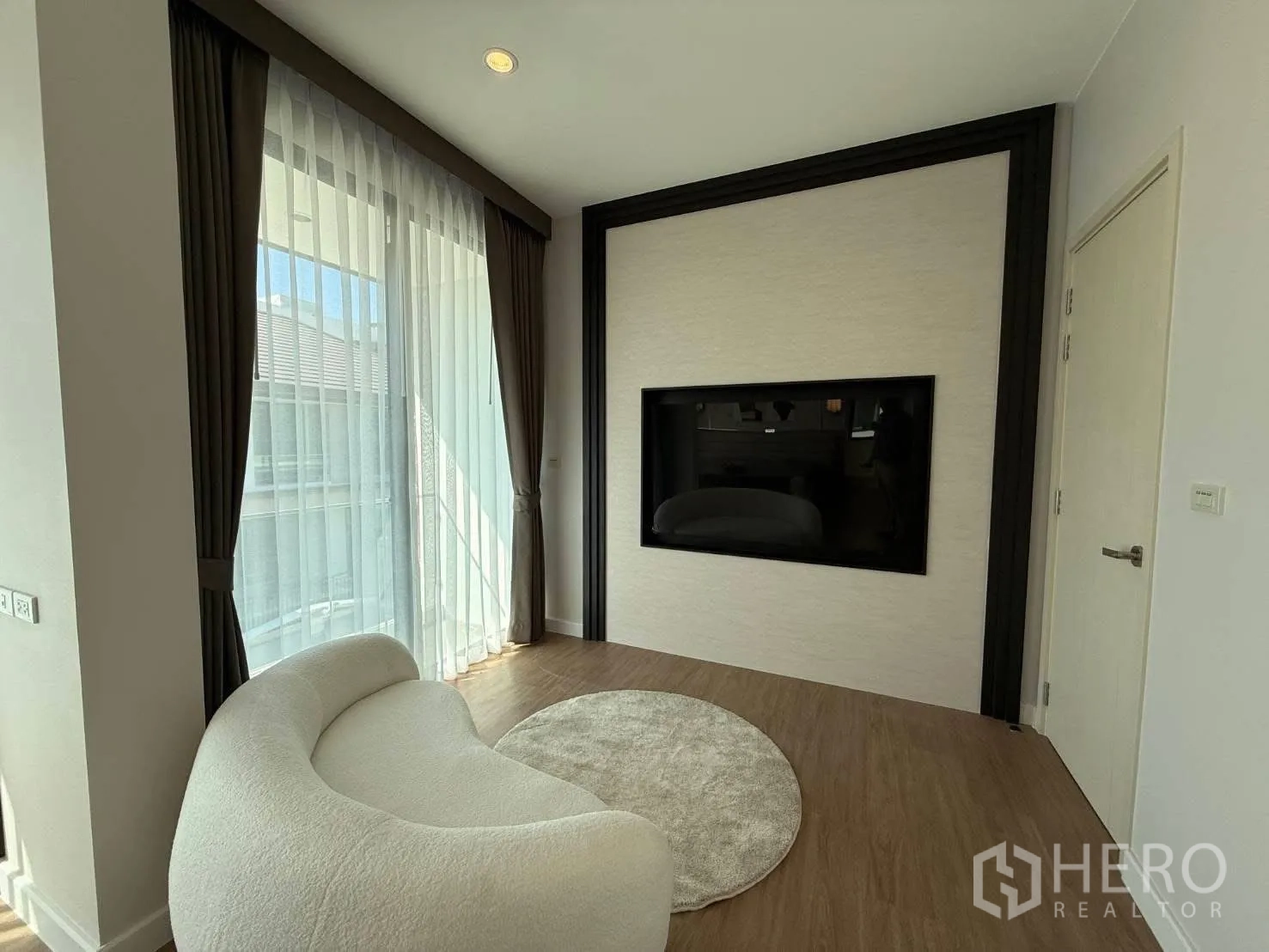 独栋房屋 for rent in Bang Phli, Samut Prakan - 明亮休闲角，弧形米色沙发、大窗帘与嵌入式电视墙。