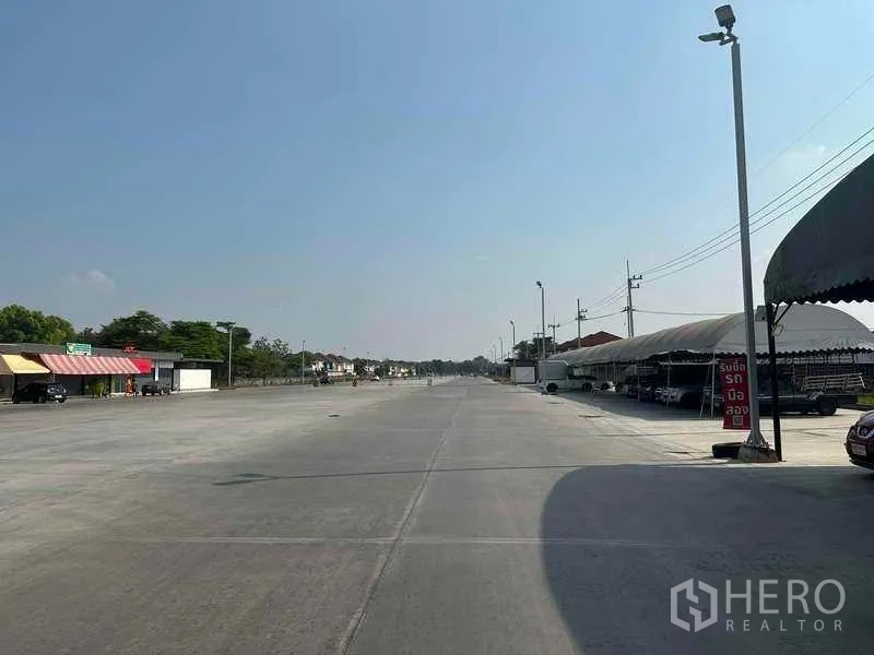 Retail Space for rent in Pathum Thani - Expansive paved area with tented stalls on the right and shopfronts on the left, ideal for parking.
