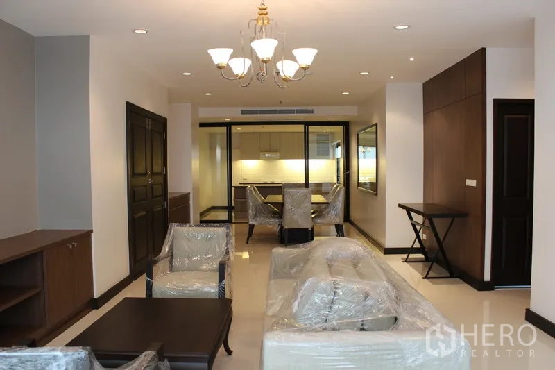 คอนโด ให้เช่าในWatthana, Bangkok - โถงนั่งเล่นรับประทานอาหารพร้อมโคมระย้า เฟอร์นิเจอร์ใหม่ห่อพลาสติก มองเห็นครัวปิดกระจก