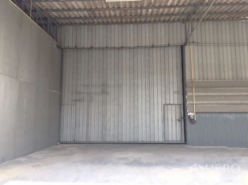 Warehouse for rent in Prawet, Bangkok - Interior of warehouse with large corrugated metal sliding door and smooth concrete floor.