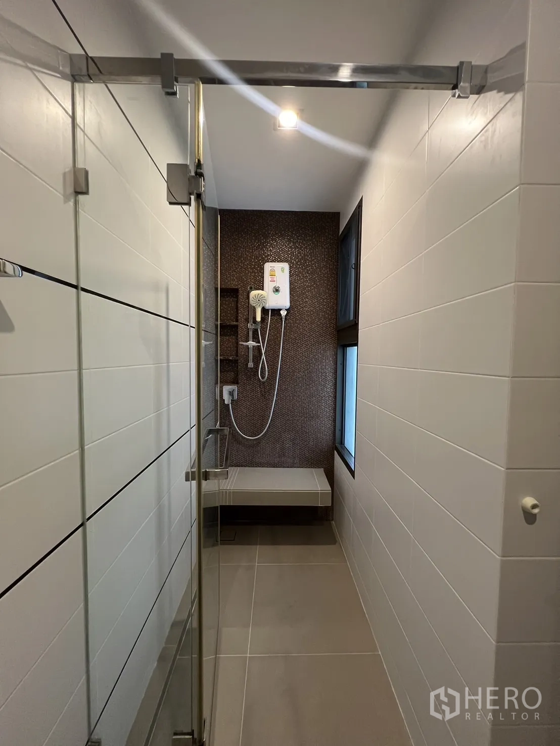 Townhouse for rent in Lat Phrao, Bangkok - Narrow shower room with glass door, tiled walls and electric shower unit.
