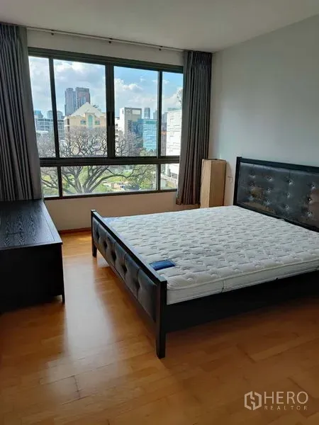 Condominium for sale in Khlong Toei, Bangkok - Bright bedroom with large window, city and green views, wood floors and upholstered bed.