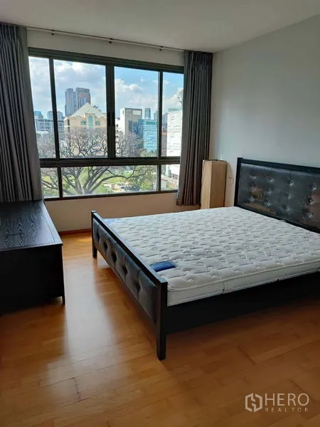 Condominium for sale in Khlong Toei, Bangkok - Bright bedroom with large window, city and green views, wood floors and upholstered bed.