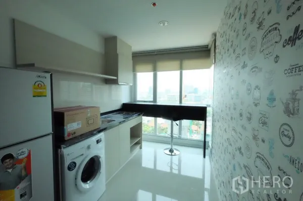 Condominium for rent in Sathon, Bangkok - Windowed kitchen with fridge, washing machine, upper cabinets and a bar counter overlooking the Bangkok skyline.
