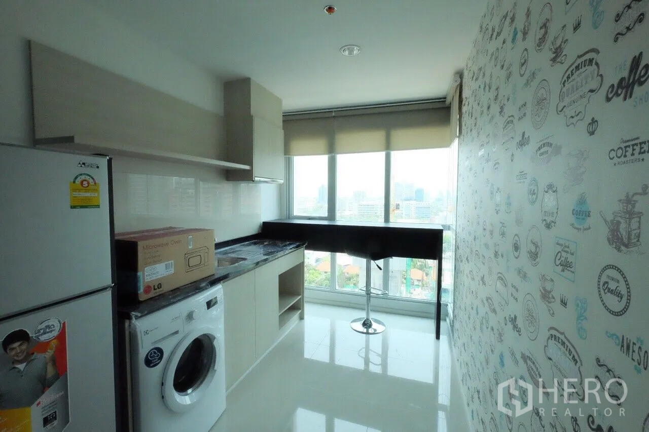 Condominium for rent in Sathon, Bangkok - Windowed kitchen with fridge, washing machine, upper cabinets and a bar counter overlooking the Bangkok skyline.
