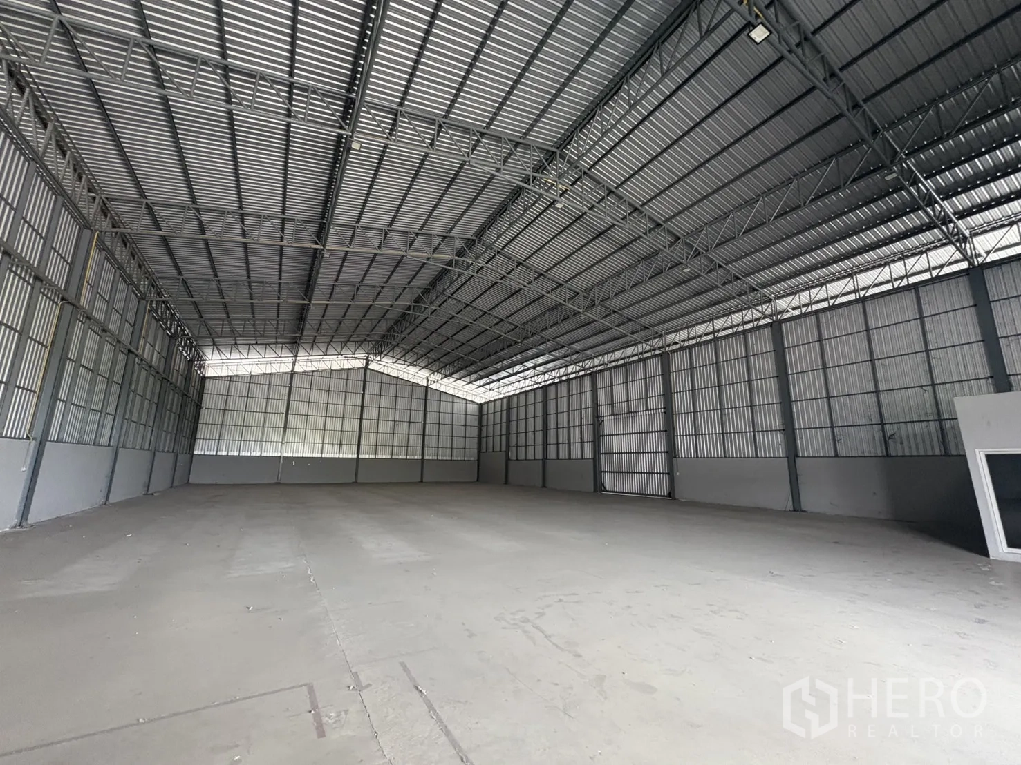 Warehouse for rent in Mueang Samut Prakan, Samut Prakan - Wide interior shot highlighting clear‑span structure, ridge skylight panels and large loading door at the end.