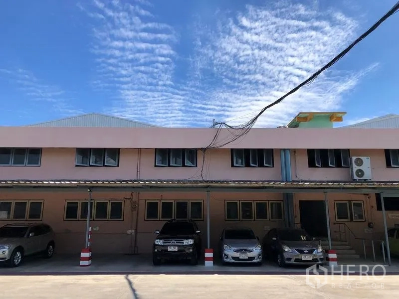 คลังสินค้า ให้เช่าในNonthaburi - อาคารสำนักงานด้านหน้า มีที่จอดรถมีหลังคาพร้อมรถหลายคันใต้ท้องฟ้าสีฟ้า