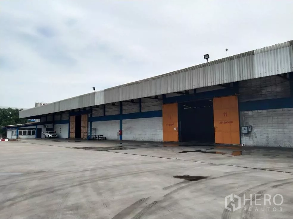 Factory for rent in Samut Prakan - Factory exterior showing wide concrete yard, covered loading bays and large sliding doors with ample truck access in Phra Pradaeng.