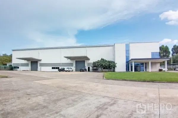 Factory for sale in Rayong - Modern white factory exterior in Pluak Daeng, Rayong with two loading bays, office wing, wide driveway and lawn.