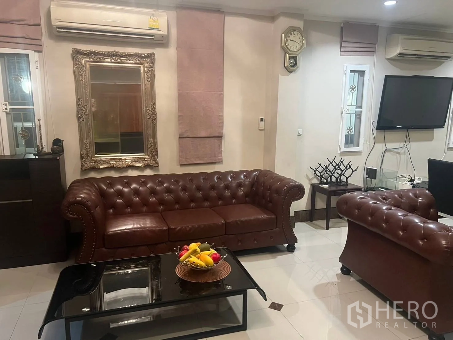 บ้านเดี่ยว for rent in Pak Kret, Nonthaburi - มุมนั่งเล่นพร้อมชุดโซฟาเชสเตอร์ฟิลด์ ทีวีติดผนัง กระจกตกแต่ง และเครื่องปรับอากาศ