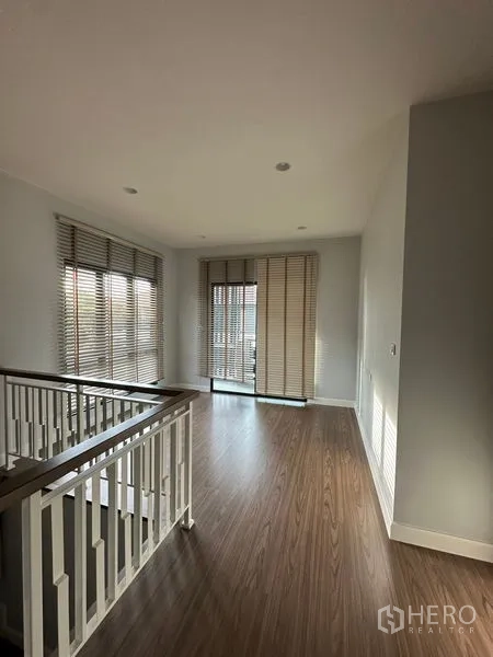 Detached House for rent or sale in Lam Luk Ka, Pathum Thani - Bright upper landing with large windows, blinds and a balcony door over wood floors.