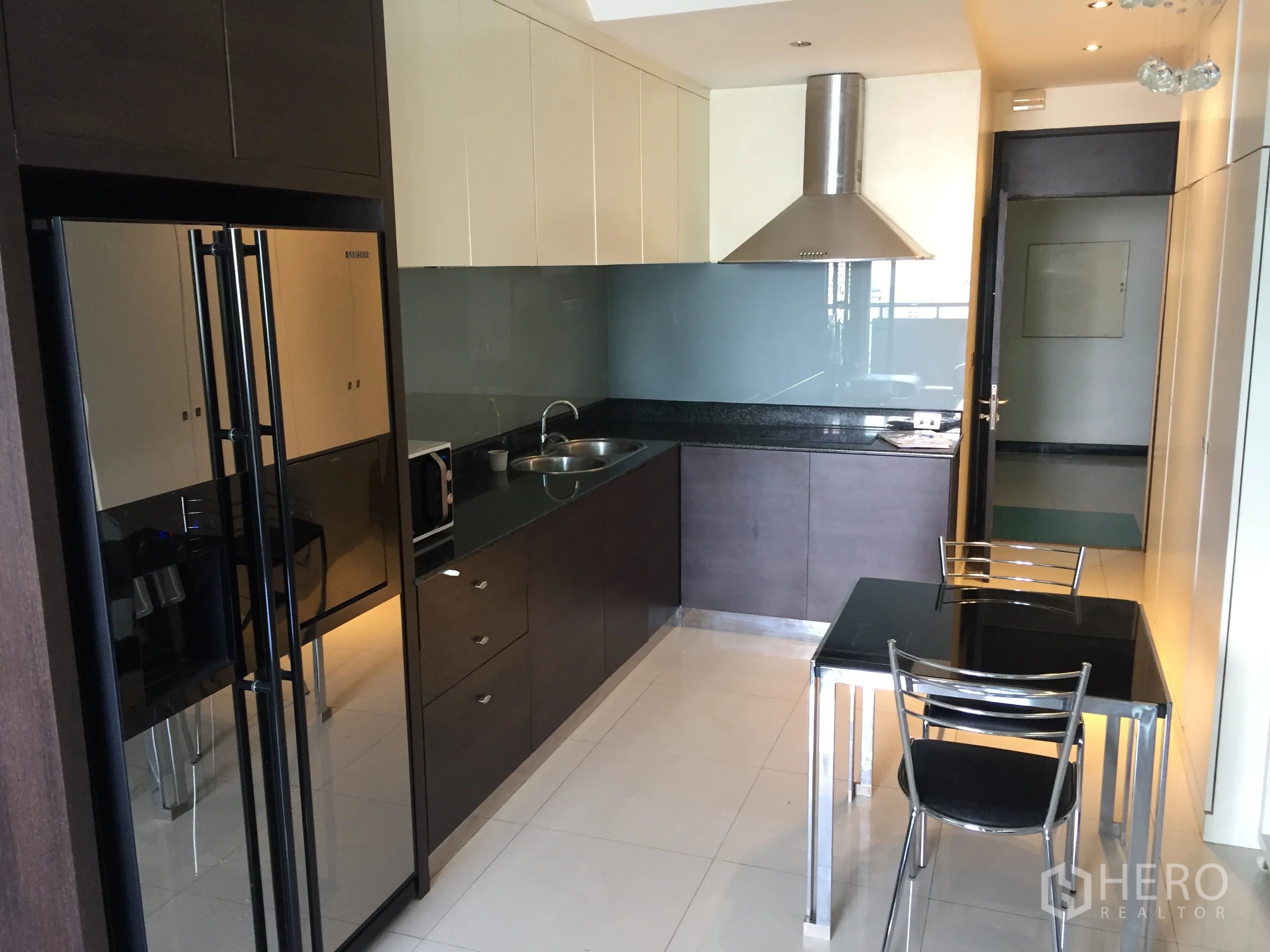 Condominium for rent in Bang Rak, Bangkok - Modern kitchen with stone countertop, stainless hood, double-door fridge and a two-seat dining table.