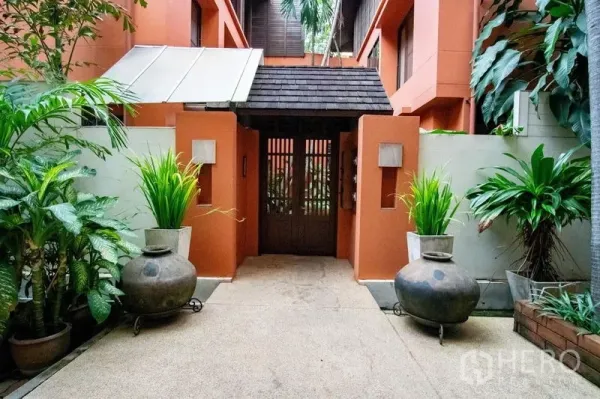 Townhouse for rent in Watthana, Bangkok - Tropical townhouse entrance with terracotta walls, wooden gate, and potted plants in Watthana.