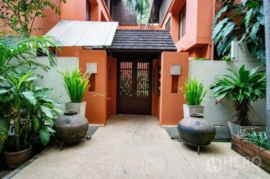ทาวน์เฮาส์ ให้เช่าในWatthana, Bangkok - ประตูทาวน์เฮ้าส์สไตล์ทรอปิคอล ผนังสีอิฐและประตูไม้พร้อมกระถางต้นไม้ ในเขตวัฒนา