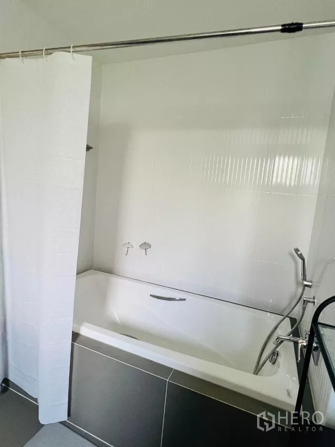 Detached House for rent in Saphan Sung, Bangkok - Bathroom with white bathtub, shower curtain and handheld shower.
