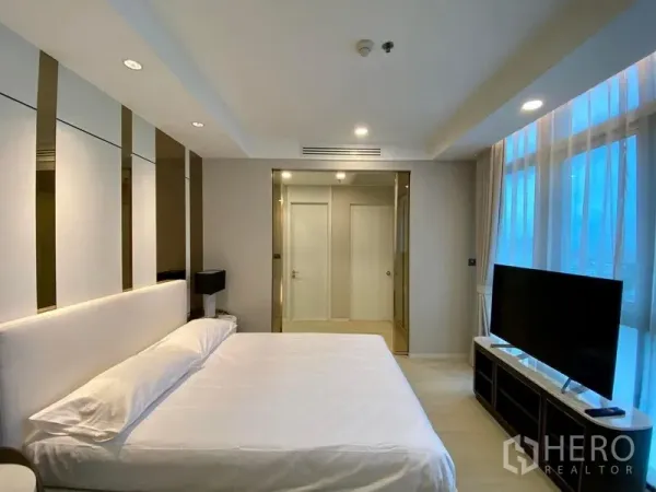 Condominium for rent in Khlong Luang, Pathum Thani - Primary bedroom with king bed, wall paneling, TV console and floor-to-ceiling windows at Nusasiri Grand Condo, Khlong Toei.