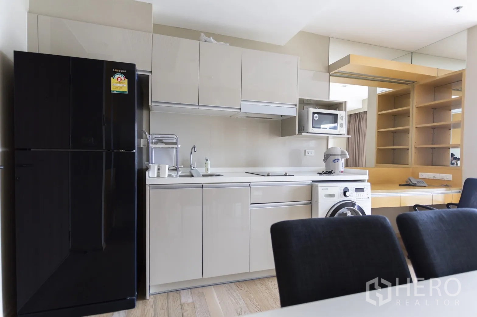 Condominium for rent in Khlong Toei, Bangkok - Modern compact kitchen with glossy cabinets, black fridge, microwave, cooktop and washing machine.